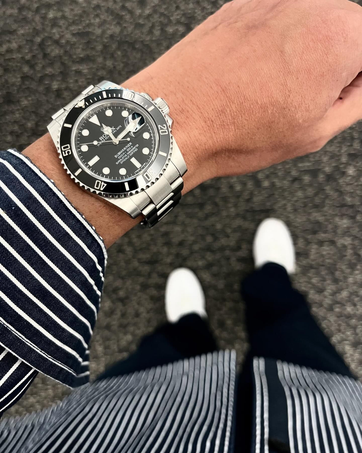 Rolex Submariner replica con quadrante e lunetta neri, indossato al polso con camicia a righe – Tre Lancette